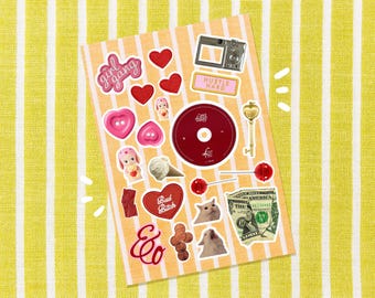 May include: A sticker sheet featuring diverse designs such as hearts, a camera, a key, and a dollar bill. The stickers display text including "girl gang", "Hustle Hard", and "Bad Bitch". The background is a yellow and white striped pattern.