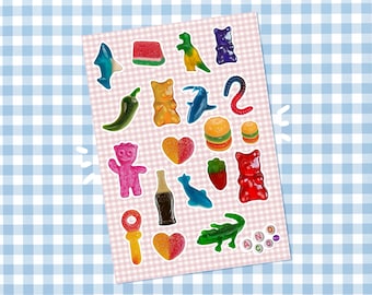 May include: A sheet of colorful gummy candies in various shapes, including a shark, dinosaur, gummy bear, and heart. The candies are arranged on a pink and white checkered background, with the letters "AND CO" at the bottom.