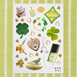 Puede incluir: Una colección de amuletos y símbolos de la suerte, que incluyen un gato Maneki-neko, tréboles de cuatro hojas, herraduras y una galleta de la fortuna. La imagen también presenta un reproductor de MP3 verde y una caja de joyería decorativa. El fondo es un patrón de rayas verdes y blancas.