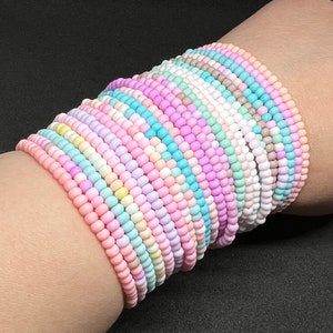 May include: A stack of pastel-coloured beaded bracelets, each with a different colour combination. The bracelets are made of small, round beads and are arranged in a neat pile on a person's wrist.