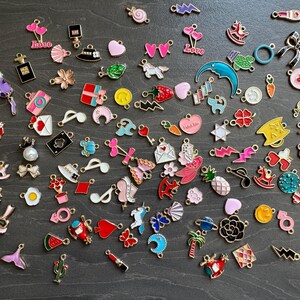 May include: A collection of colourful enamel charms featuring various designs, including hearts, stars, animals, and abstract shapes. The charms are perfect for adding a touch of personality to jewellery, keyrings, or other crafts.