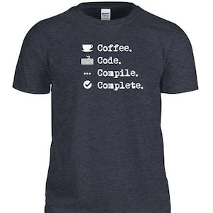 May include: A dark blue t-shirt with a white graphic that reads "Coffee. Code. Compile. Complete."