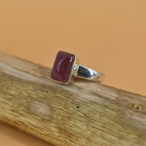 May include: A silver ring with a rectangular, deep pink gemstone.