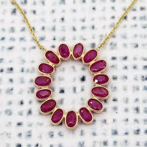 May include: A gold chain necklace with a pendant made of a circle of oval-shaped ruby gemstones.
