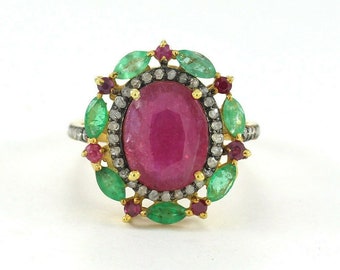 May include: A gold ring with a large oval ruby surrounded by a halo of smaller diamonds and emeralds. The ring is set with smaller rubies and emeralds around the halo.