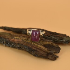 May include: A silver ring with a rectangular, deep pink gemstone.