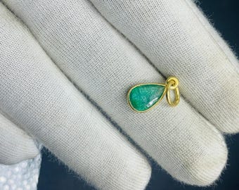 May include: A teardrop-shaped emerald pendant charm with a gold setting. The pendant is on a white surface.