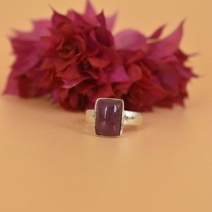 May include: A silver ring with a rectangular, deep purple gemstone.
