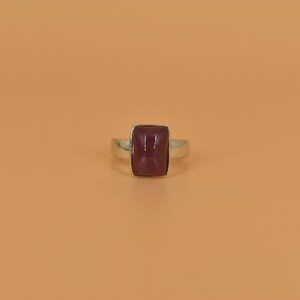 May include: A silver ring with a rectangular, dark purple gemstone.