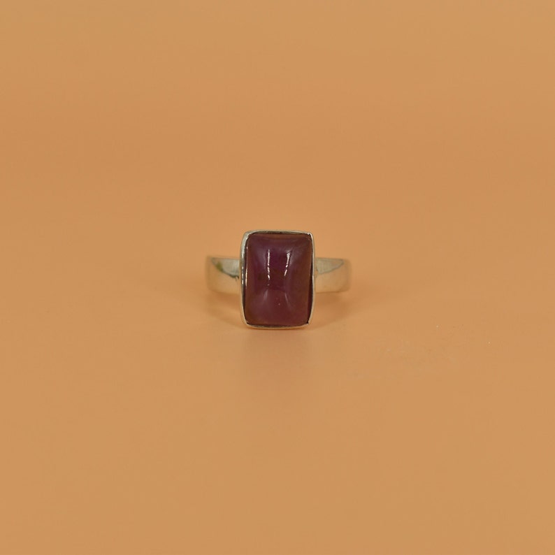 May include: A silver ring with a rectangular, dark purple gemstone.