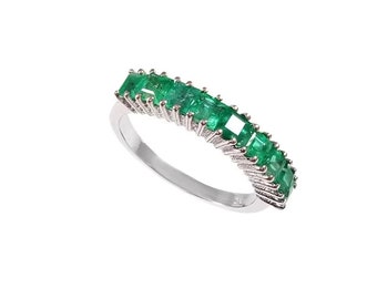 May include: A silver band ring with a row of emerald green square-shaped gemstones set in a prong setting.