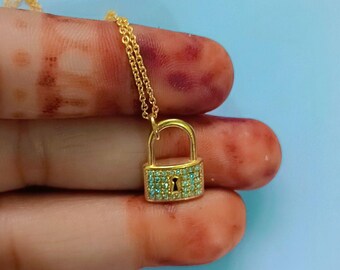 May include: A gold chain necklace with a small padlock pendant. The padlock is covered in tiny blue gemstones.