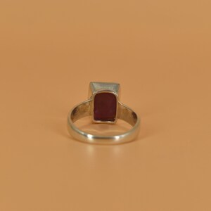May include: A silver ring with a rectangular, dark red gemstone.