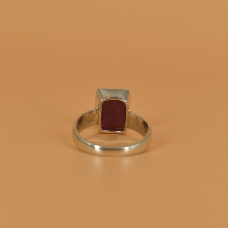 May include: A silver ring with a rectangular, dark red gemstone.