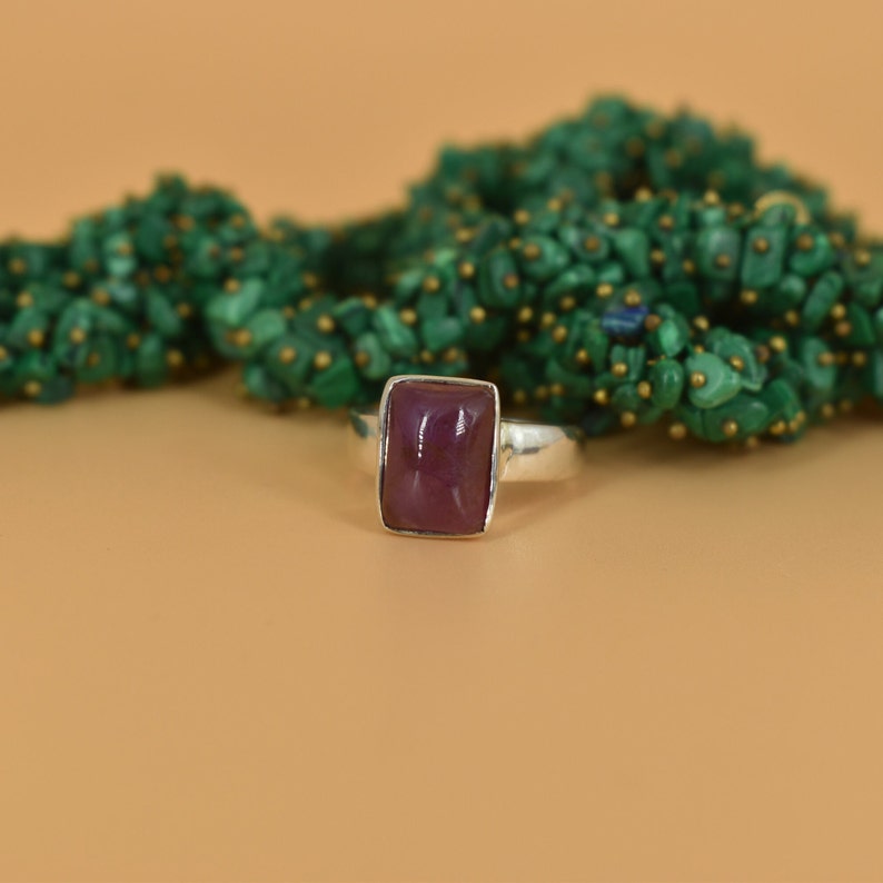 May include: A silver ring with a square, dark purple gemstone.