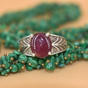 Peut inclure: Une bague en argent avec une grande pierre de rubis de forme ovale sertie au centre. La bague présente un design détaillé et orné avec des sculptures complexes.
