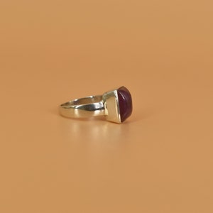 May include: A silver ring with a square, dark purple gemstone.