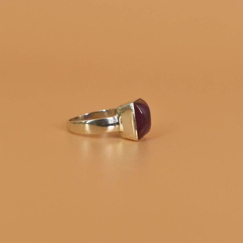 May include: A silver ring with a square, dark purple gemstone.