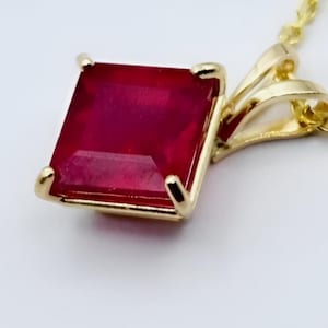 Peut inclure: Un collier pendentif en or avec une pierre précieuse rouge foncé de coupe carrée. La pierre précieuse est sertie dans une lunette en or avec quatre griffes. La chaîne est également en or.