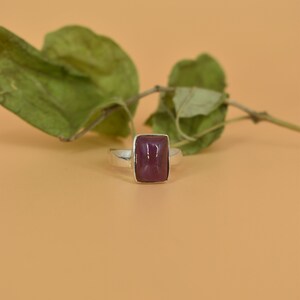 May include: A silver ring with a rectangular, dark purple gemstone.