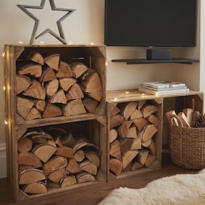 May include: Three rectangular wooden crates stacked to store firewood, featuring a natural brown finish. A large grey star ornament sits on top of the left stack, and a woven wicker basket filled with wood pieces sits beside the lower right crate.