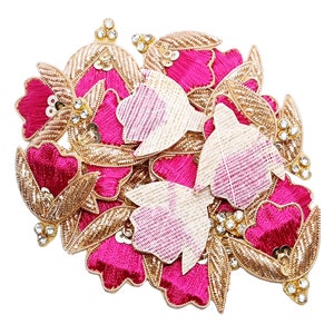 Może przedstawiać: Kolekcja ozdobnych aplikacji kwiatowych. Aplikacje mają żywe płatki w kolorze fuksji, złote haftowane liście i błyszczące akcenty z kryształków. Niektóre aplikacje mają tkany, kremowy wzór. Te dekoracyjne ozdoby są idealne do rękodzieła i zdobienia odzieży.