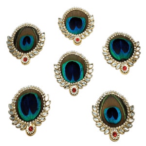 Könnte beinhalten: Sechs dekorative Pfauenfedern-Verzierungen. Jedes kreisförmige Design zeigt eine Pfauenfeder mit blauen und grünen Farbtönen, umgeben von einem goldfarbenen Rahmen mit klaren Strasssteinen. Ein kleiner roter Edelstein akzentuiert den Boden jedes Stücks.