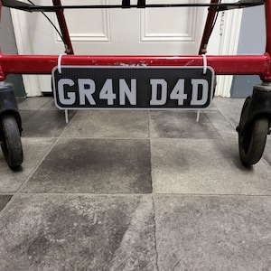 May include: A black and white number plate with the text "GR4N D4D" hanging from a red metal frame.