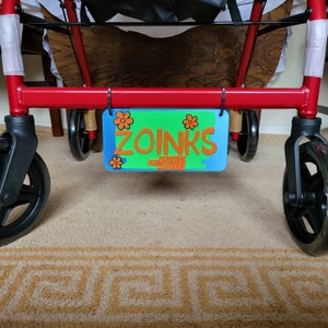 May include: A red walker with a blue and green sign that says "Zoinks! The Mystery Machine" with orange flowers on the sign.