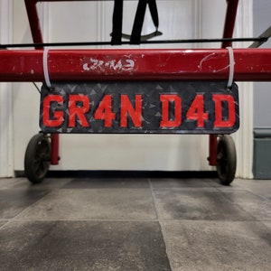 May include: A red metal bar with a black and white number plate that says "GR4N D4D" hanging from it.