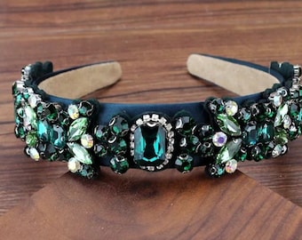 May include: A dark green velvet headband with a large emerald green rhinestone design. The headband is decorated with smaller rhinestones in various shades of green.