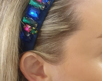 May include: A blue velvet headband with colorful jewels and a large blue gemstone in the center.