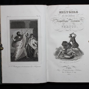 May include: An open book with illustrations and French text. The left page features a black and white engraving of figures in classical attire. The right page displays the title "Histoire des Révolutions en la République Romaine" and another illustration.