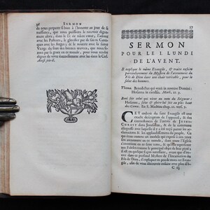 May include: An open book with text and illustrations. The left page has a decorative bowl of fruit. The right page features the title "SERMON POUR LE I LUNDI DE L'AVENT" in large text. The book is held by a bronze hand.