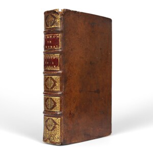 May include: A vintage, leather-bound book with gold accents. The spine features red panels with gold lettering and decorative elements. The book's cover is a rich brown color, and the edges show signs of wear, suggesting its age.