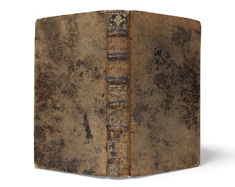 May include: A vintage book with a worn, brown leather cover. The spine features gold decorative elements and text. The book's edges are slightly rounded, and the overall appearance suggests age and use.