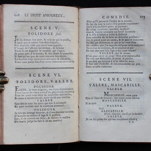 K&ouml;nnte beinhalten: Ein offenes antikes Buch mit gealterten, vergilbten Seiten. Der Text ist auf Franz&ouml;sisch, mit dem Titel "LE DEPIT AMOUREUX" sichtbar. Das Buch wird von verzierten Metallbuchst&uuml;tzen gehalten.