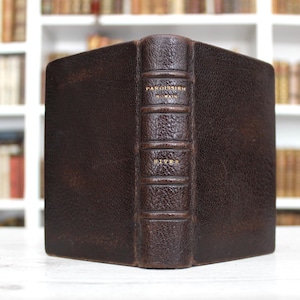 Könnte beinhalten: Ein dunkelbraunes, ledergebundenes Buch mit strukturierter Oberfläche und erhabenen Bünden am Buchrücken. Auf dem Rücken befindet sich goldgeprägter Text mit der Aufschrift PAROISSIEN ROMAIN und HIVER. Das Buch steht aufrecht.