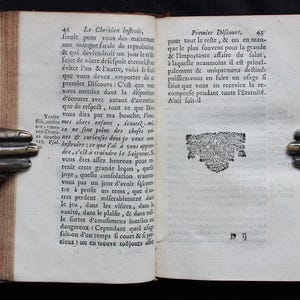 Pode incluir: Um livro aberto com um desenho decorativo na p&aacute;gina direita. O texto na p&aacute;gina esquerda diz: "Le Chrisien inftrvis, feroit pour vous des maintenan une marque fatale de reprobatin, & qui deviendroit un jour le t fujet de votre defeſpoir &eacute;ternel. Por &eacute;viter l'un & l'autre, voici le fut que vous devez empotter de a premier Difcours: C'est que vou vous mettiez dans la difpofisis d'&eacute;couter avec autant d'attentiu que de refpect, tout ce que Din Venite vous dira par ma bouche. Fo Fin, audite mes chers enfans &eacute;coutez mi mco ne font point des choses so ni docebo nes & curieuses dont je veux vo Pial inftruire ce que j'ai &agrave; vous appro dre, c'est &agrave; craindre le Seigneur. vous &ecirc;tes allez heureux pour tenir cette grande le&ccedil;on, quri joye, quelle confolation n'art vous pas un jour d'avoir f&ccedil;um tre &agrave; profit un rems, que di tres perdent miferablement dati le jeu, dans les vifites, dans vanit&eacute;, dans le plaifir, && dans mi le fortes d'amufemens inutiles of dangereux Cependant quel ulaga fait-on d'un temps fi court & fi po cicux on en trouve to&ucirc;jours a"