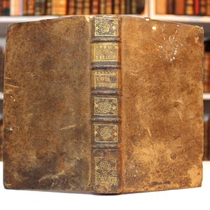 Könnte beinhalten: Ein antikes, ledergebundenes Buch mit goldenen Verzierungen und dem Titel "Œuvres de J.J. Rousseau" auf dem Rücken.