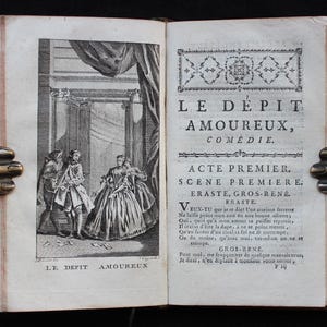 K&ouml;nnte beinhalten: Ein aufgeschlagenes antikes Buch mit einer Schwarz-Wei&szlig;-Illustration auf der linken Seite und franz&ouml;sischem Text auf der rechten Seite. Die Illustration zeigt drei Figuren in einem klassischen Rahmen. Der Buchtitel lautet "LE D&Eacute;PIT AMOUREUX."