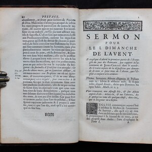 May include: Open antique book with text in French. The pages are aged and yellowed, with visible text and ornate decorative elements. The book is open to a page with the title "SERMON POUR LE I DIMANCHE DE L'AVENT."