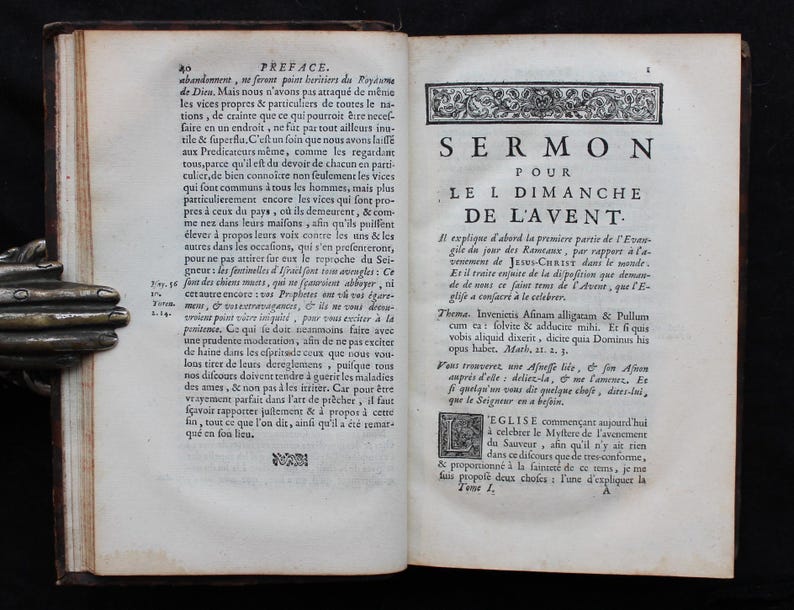 May include: Open antique book with text in French. The pages are aged and yellowed, with visible text and ornate decorative elements. The book is open to a page with the title "SERMON POUR LE I DIMANCHE DE L'AVENT."