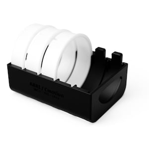 Peut inclure: Un boîtier en plastique noir contenant trois anneaux blancs. Le boîtier porte l'inscription "ARAI / Emotion WCU - HIS + CPD" sur le côté.