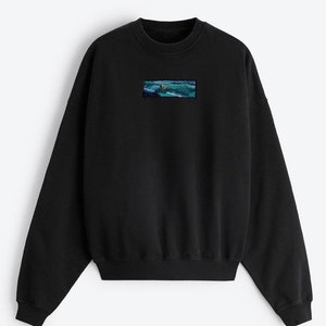 Op de afbeelding: Zwart sweatshirt met een klein geborduurd beeld van een zeezicht op de voorkant.