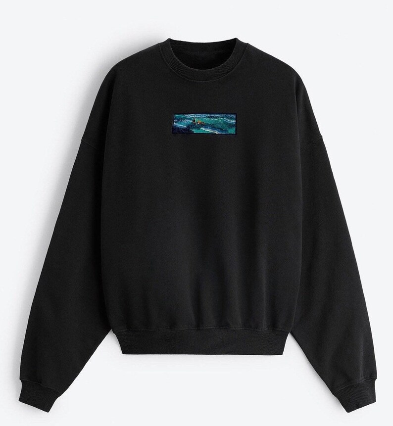 Op de afbeelding: Zwart sweatshirt met een klein geborduurd beeld van een zeezicht op de voorkant.