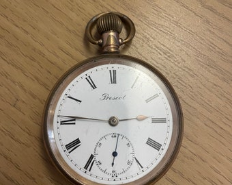 May include: A gold pocket watch with Roman numeral markings on the face. The watch face reads "Prescot".
