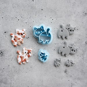 May include: A set of cookie cutters featuring a cat design. The cutters are made of blue and gray plastic. There are two larger cutters and four smaller cutters.