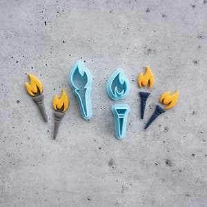 May include: A set of six blue plastic cookie cutters shaped like torches. The cutters are arranged on a gray textured surface.