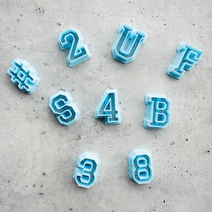 May include: A set of nine blue plastic cookie cutters shaped like letters and numbers. The letters are U, F, B, and S. The numbers are 2, 4, 3, and 8.